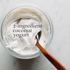 a jar filled with yogurt sitting on top of a white counter next to a wooden spoon