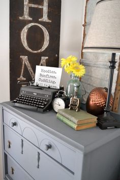 a desk with a typewriter, lamp and flowers on it next to a wooden sign