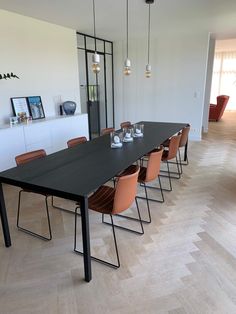 a long table with orange chairs in the middle of a room that has white walls and wood flooring