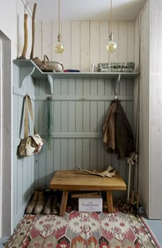 a wooden bench sitting under two hanging lights next to a wall with coat hooks on it