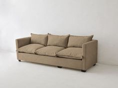 a tan couch sitting in front of a white wall with two pillows on top of it