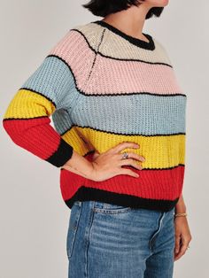 a woman wearing a multicolored sweater with her hands on her hips and looking off to the side