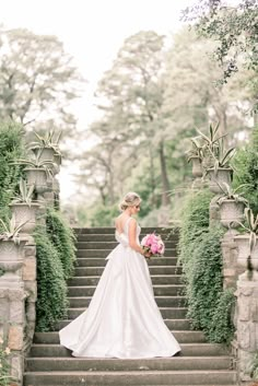 a woman in a wedding dress is standing on some steps with flowers and greenery