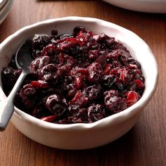 a white bowl filled with cranberry sauce on top of a wooden table next to silverware