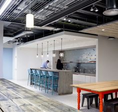 an open kitchen and dining area with wooden tables, blue stools and white walls