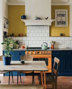 a kitchen with blue cabinets, yellow walls and a wooden table in front of the stove