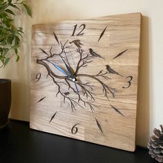 a wooden clock with birds on it sitting next to a potted plant