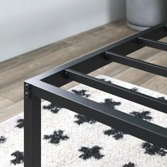 a black metal bed frame sitting on top of a white carpeted floor next to a vase