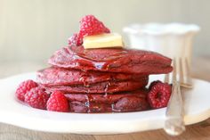 a stack of pancakes with raspberries and butter on top sitting on a white plate