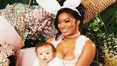 a woman holding a baby wearing bunny ears and sitting in front of some fake flowers