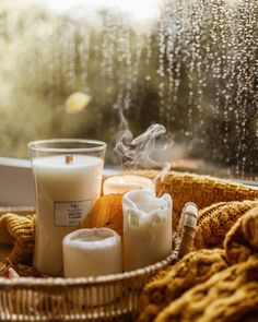 some candles are sitting in a wicker basket by a window with rain coming down