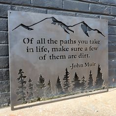 a metal sign on the side of a building with trees and mountains in it that says, off all the paths you take in life, make sure a few of them are dirt