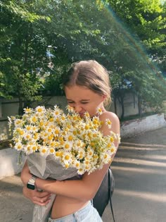 a woman holding a bunch of daisies in her arms