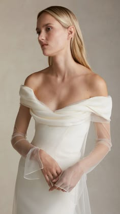 a woman wearing a white wedding dress with sheer sleeves on her shoulder and veil over her head