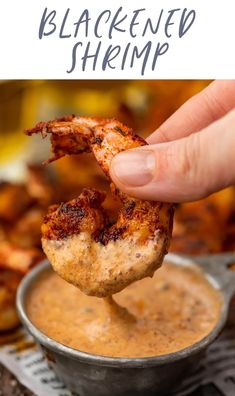 a hand holding up a piece of grilled shrimp over a bowl of dipping sauce