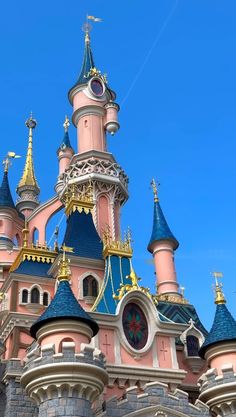 a pink and blue castle with gold trim on it's roof is seen against a blue sky