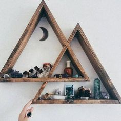 someone is holding up two wooden shelves with various items on them in the shape of triangles