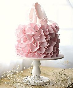 a cake with pink ruffles on top is sitting on a white pedestal in front of a window