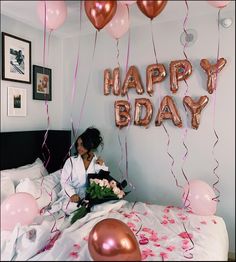 a woman is sitting on her bed with balloons and streamers in front of her