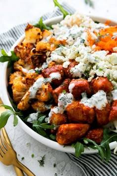 a white bowl filled with meat and vegetables on top of a table next to gold utensils