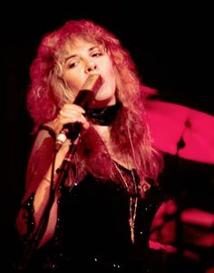 a woman singing into a microphone in front of a red light with her hair blowing back