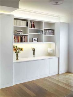 an empty room with white bookcases and flowers in vases on the counter