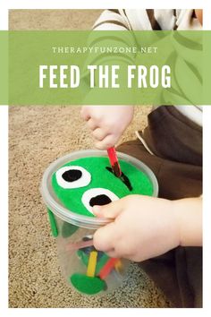 a young child is playing with a toy frog in a plastic cup that says feed the frog