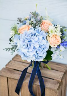 a bouquet of blue and pink flowers on a wooden crate with ribbon tied around it