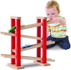 a toddler playing with a wooden toy car and track set in front of a white background