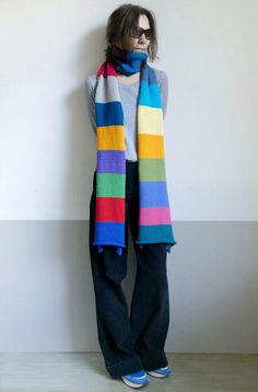 a woman standing against a wall wearing a multicolored scarf