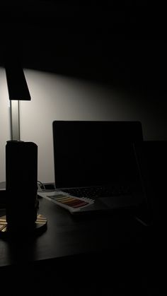 a desk with two laptops and a lamp on top of it in the dark