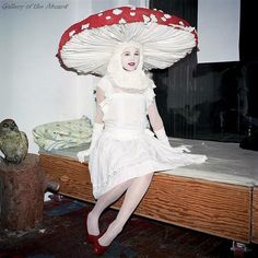 a woman in white dress sitting on top of a bed with an umbrella over her head