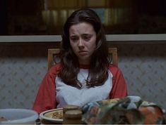 a woman sitting at a table in front of a plate with food on it and looking down