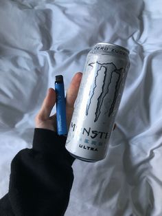 a person holding a can of energy drink and a blue pen in their left hand