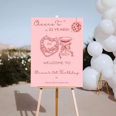 a pink welcome sign sitting on top of a wooden easel next to white balloons