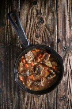 a skillet filled with stew on top of a wooden table