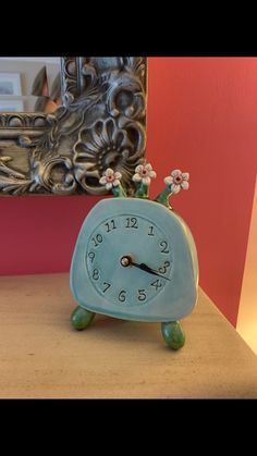 a small blue clock sitting on top of a table next to a mirror and lamp