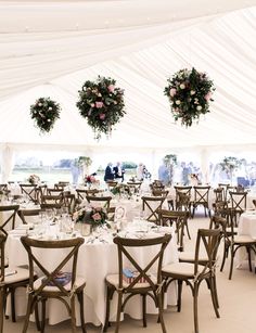 tables and chairs are set up in a tent with white linens, floral centerpieces and greenery hanging from the ceiling