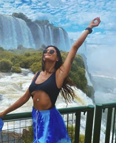 a woman standing in front of a waterfall with her arms up and hands out to the side