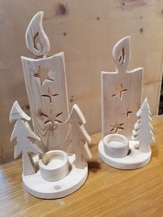 two wooden christmas trees on a table with one candle holder and the other is made out of wood