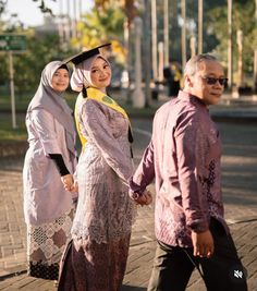 two women and a man walking down the street in hijab style attire, holding hands with each other