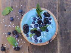 a bowl filled with blueberries and blackberries on top of a wooden table next to leaves