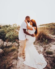 a man and woman standing next to each other on top of a sandy beach near the ocean