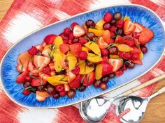 a blue plate filled with fruit on top of a red and white table cloth next to silver spoons