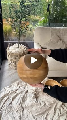 a woman sitting on a couch holding a wooden ball in front of her face and looking at it