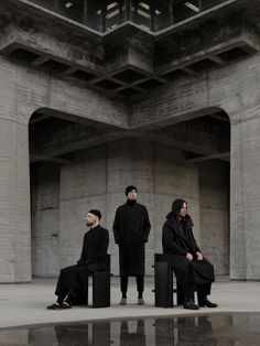 three people sitting on stools in front of a large building with columns and pillars