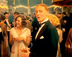 a man in a tuxedo standing next to a woman with a glass of wine