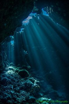 sunlight shining through the water into a cave filled with rocks and corals, underwater view