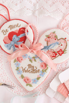 two cross stitch hearts on a doily next to some scissors and thread markers,