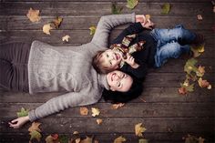 a couple laying on top of each other in front of a wooden floor covered with leaves